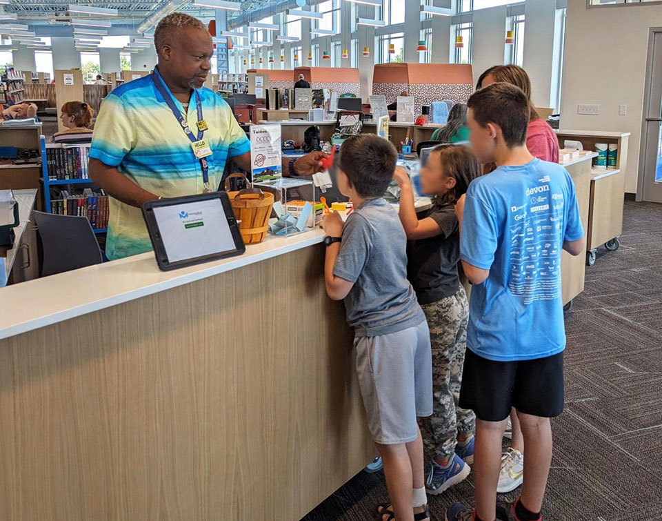 Kids at almonte library service desk asking questions in a busy library space